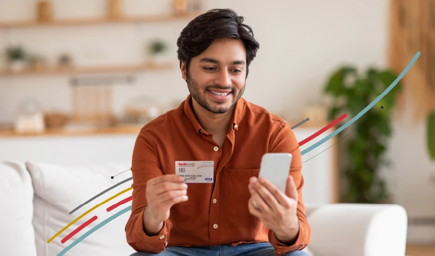 a man looking at his phone and holding a Tech CU credit card
