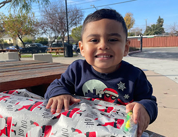a little boy is holding a present wrapped in cartoon santa paper