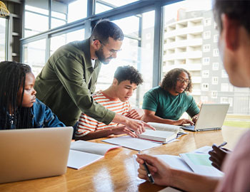 a professor shows some students work on a laptop